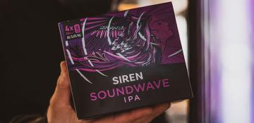 Images shows Siren Craft Brew box of Siren Soundwave IPA. The box contains four cans and the artwork on the box is of a purple 'siren' with flowing hair and wings